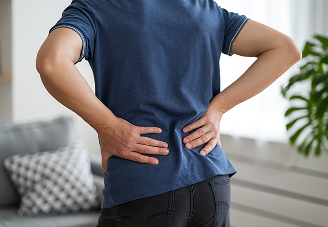 腰に痛みを感じ両手でおさえる男性